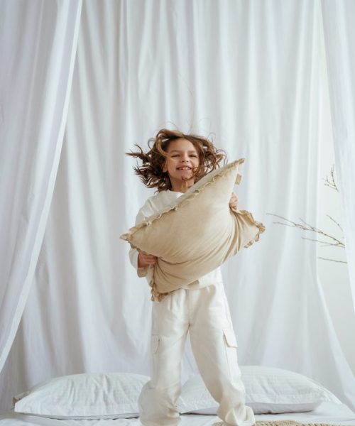 Playing with pillow on the bed. Cute little girl is at home.